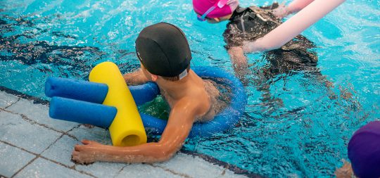 En la imagen aparecen dos niños en la piscina en un curso de natación