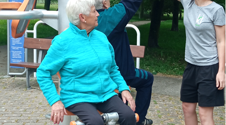 Dos ancianos hacen ejercicio en la máquina de un parque dirigidos por una monitora