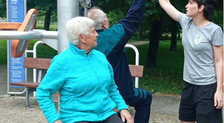 Dos ancianos hacen ejercicio en la máquina de un parque dirigidos por una monitora