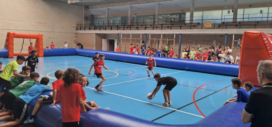 Un grupo de niños y niñas juega a futbito en una pequeña cancha con bordes y porterías de goma